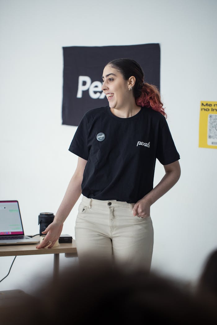 A young woman in a black T-shirt gives a presentation indoors.